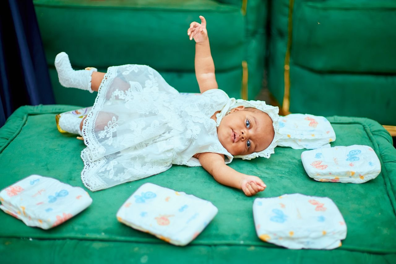 Cute baby in a white dress playing on a green sofa with diapers nearby. Ideal for childcare themes.